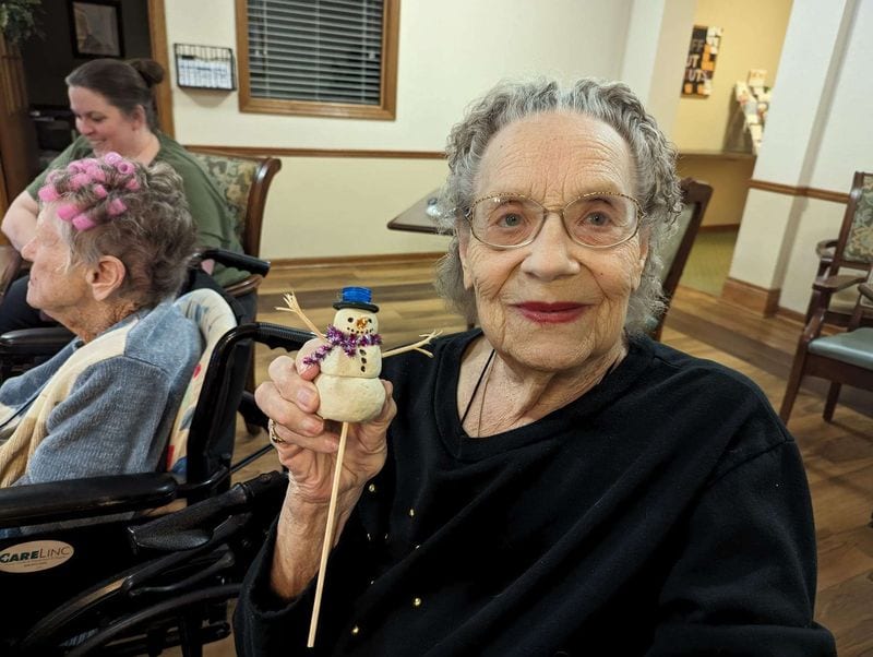 A resident smiles as she holds up the snowman she made at a craft activity
