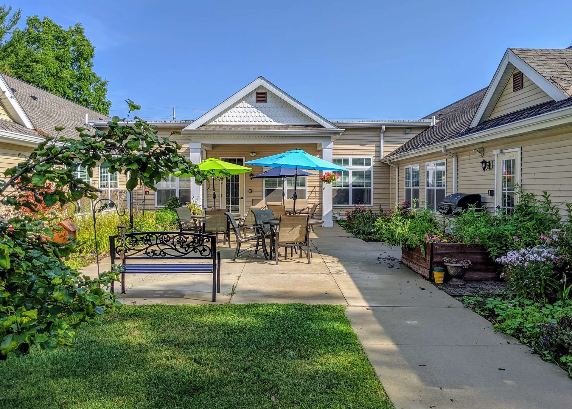 The courtyard garden at Americana Seniors of Davison, with patio tables, sun umbrellas, a bench and flower beds