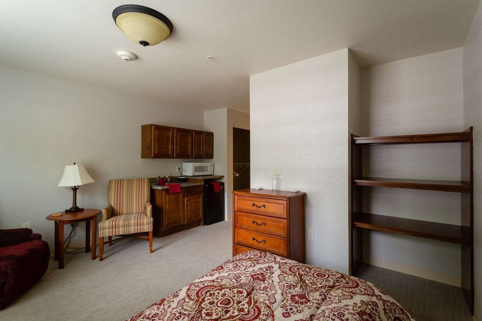 A private room with a bed, dresser and armchair