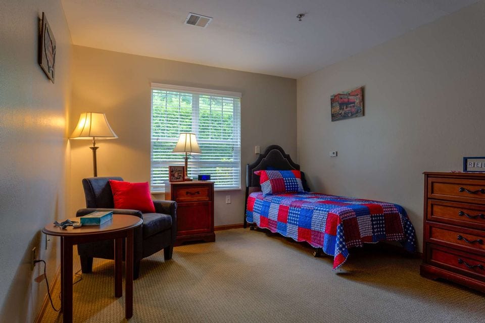 A private room with a bed, an armchair, lamps and a window